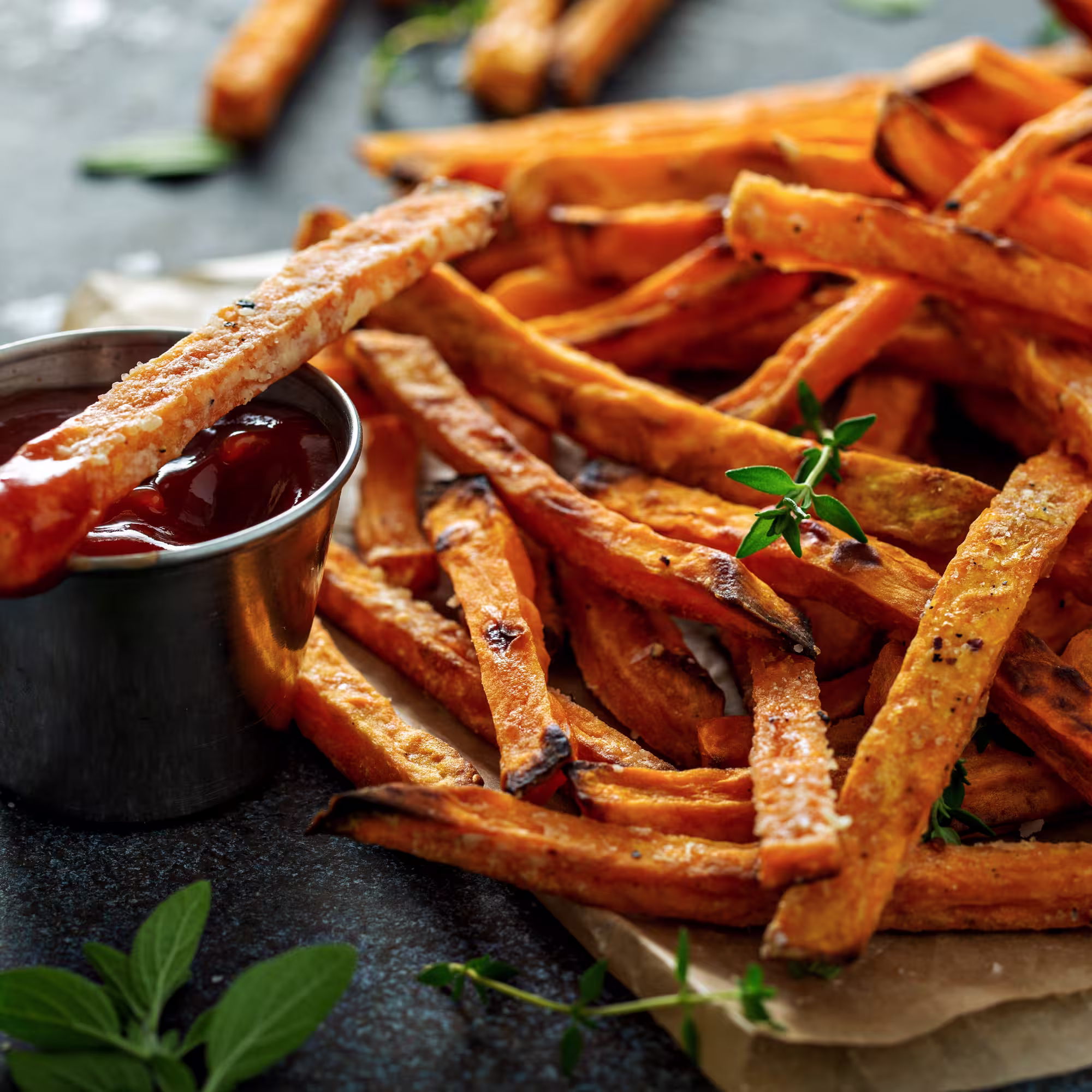 Crispy sweet potato fries served with ketchup and garnished with fresh herbs.