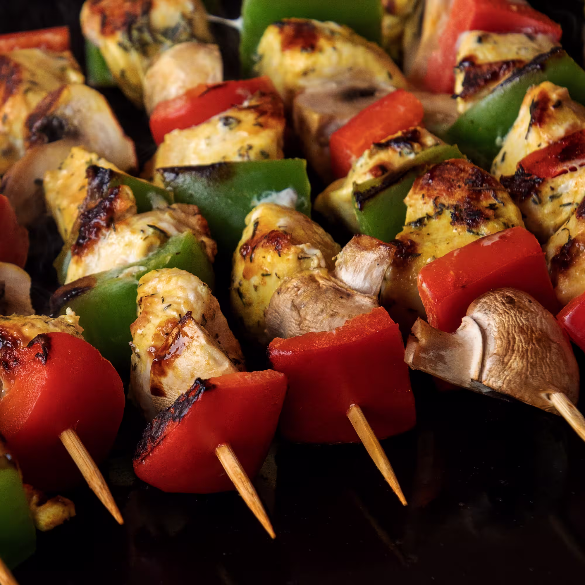 Grilled chicken, green bell pepper, red bell pepper, and mushroom skewers with char marks.