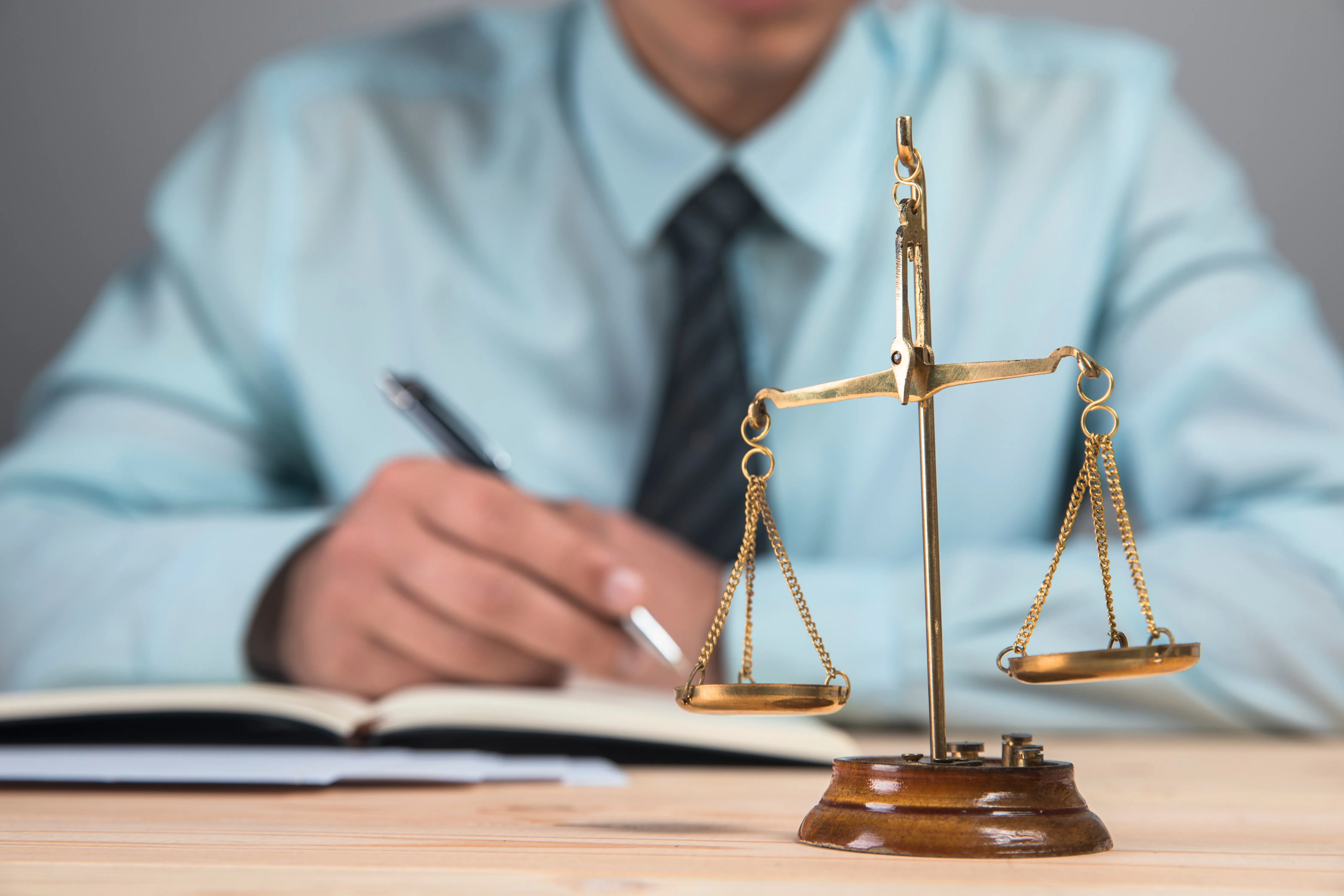 Scales of justice on desk with person writing in background