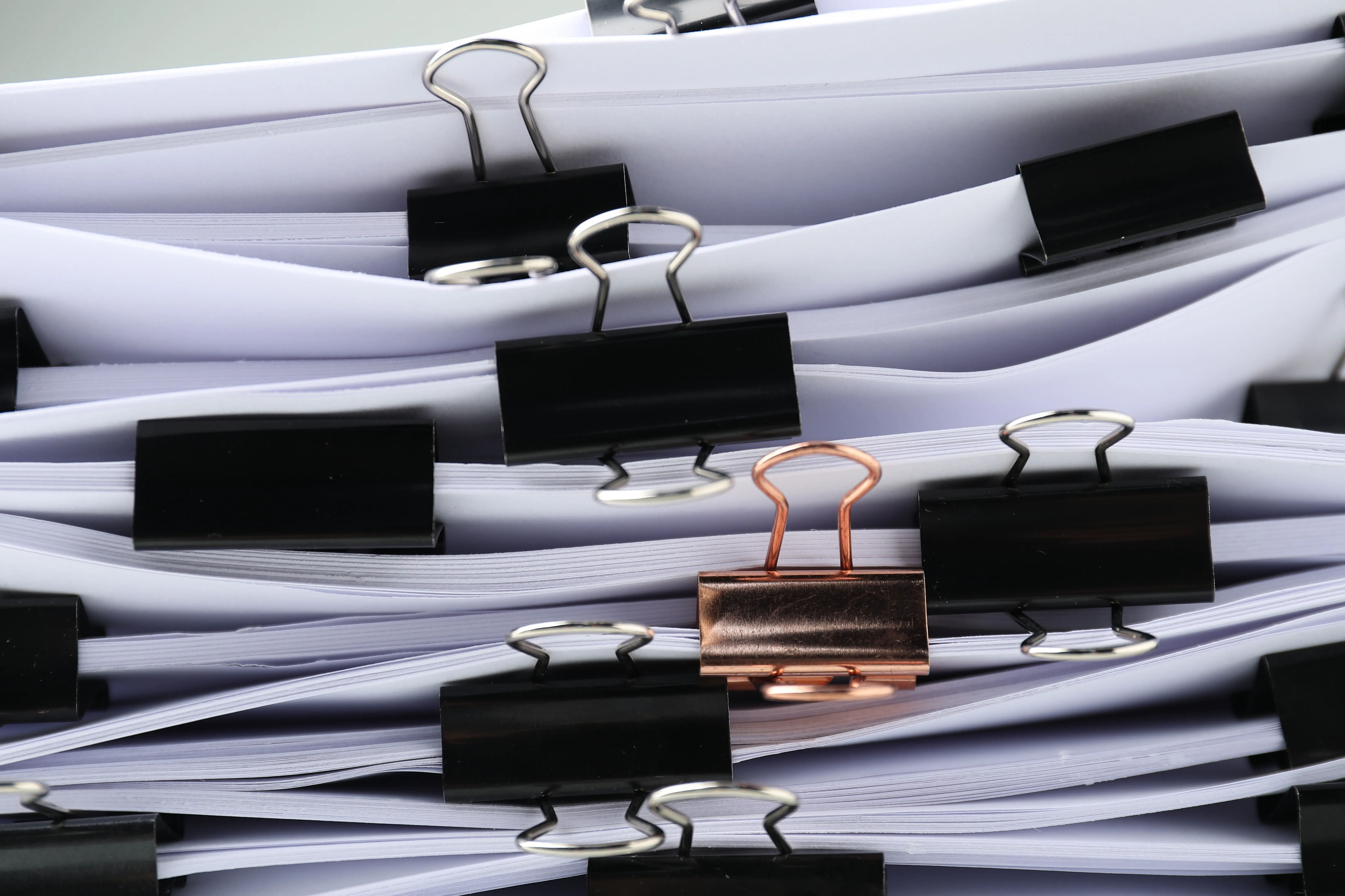 Black and copper binder clips fastening stacked white paper documents