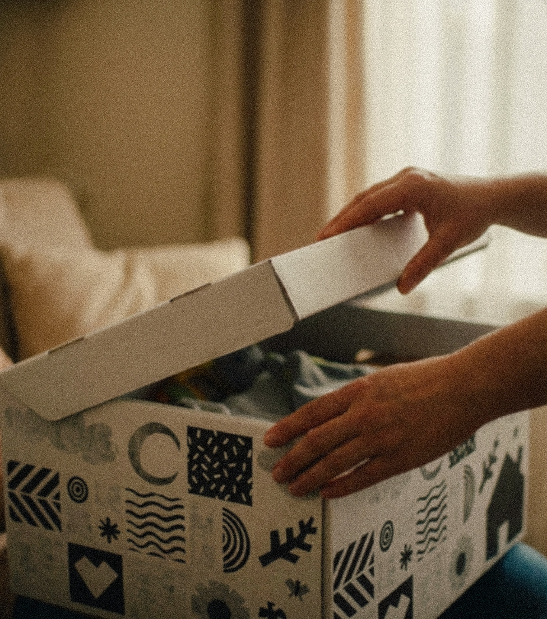 Person lifting the lid off a patterned box with black and white abstract designs on it.