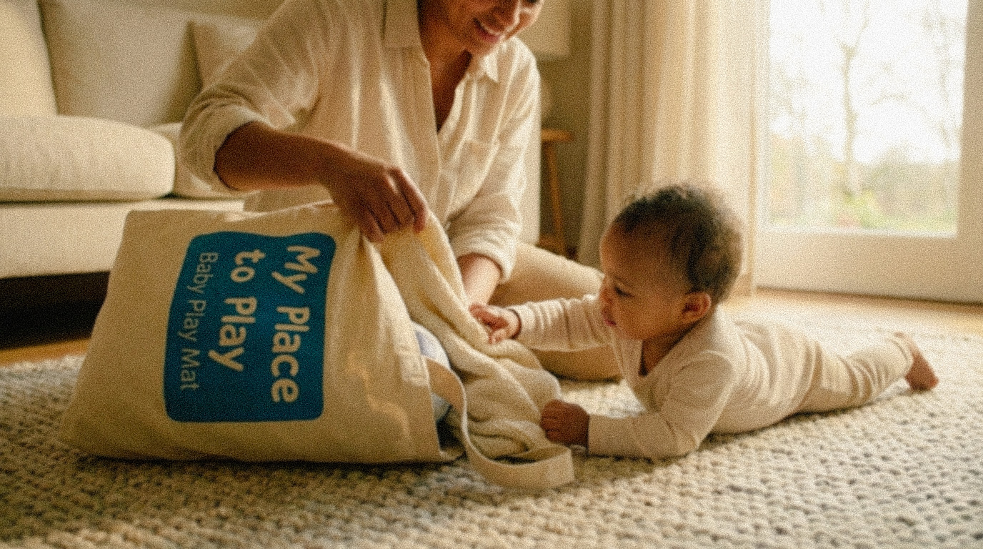 Smiling woman unpacking a baby play mat from a tote bag while a baby reaches out on a carpeted floor.