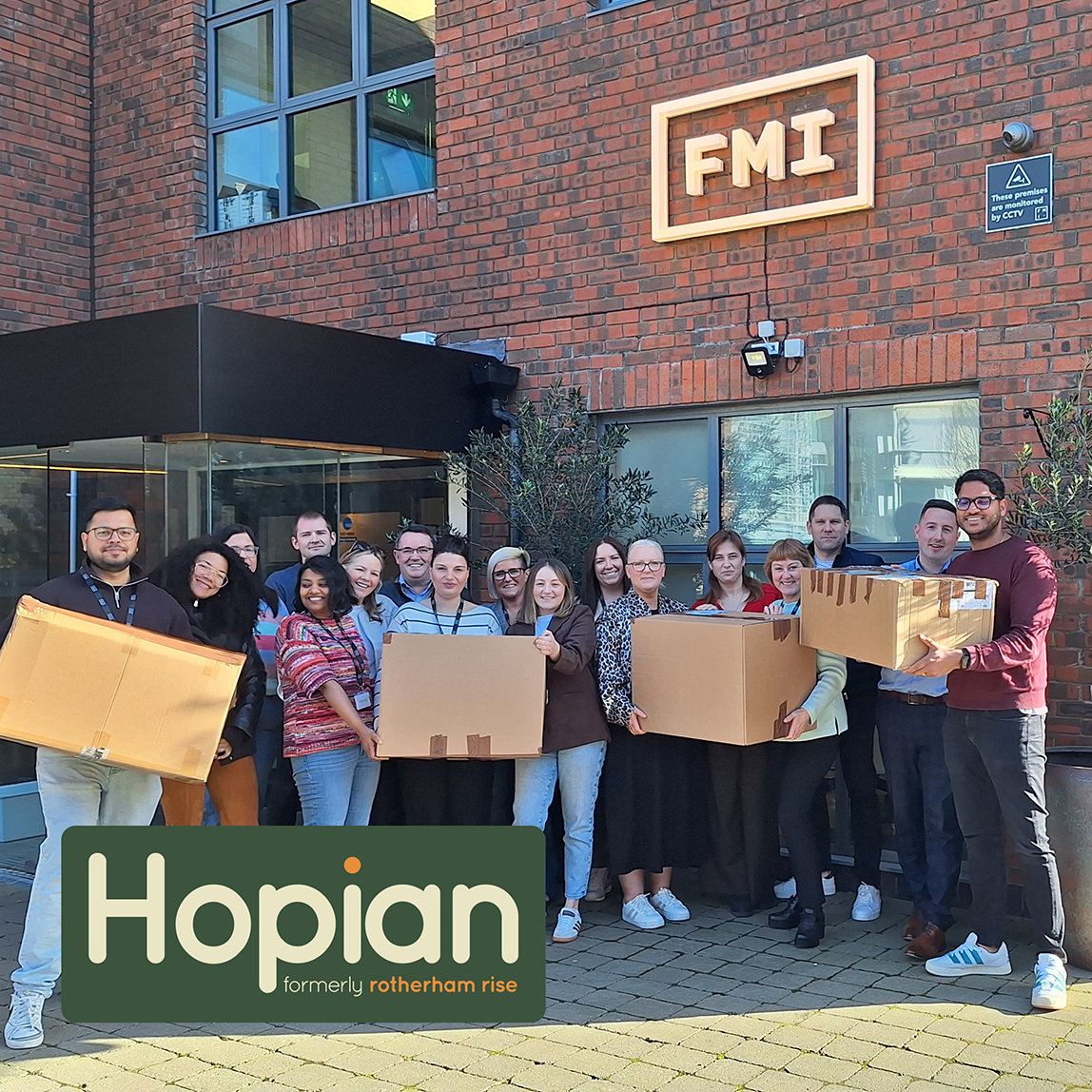 Diverse group of people standing outside a brick building holding large cardboard boxes under an FMI sign.