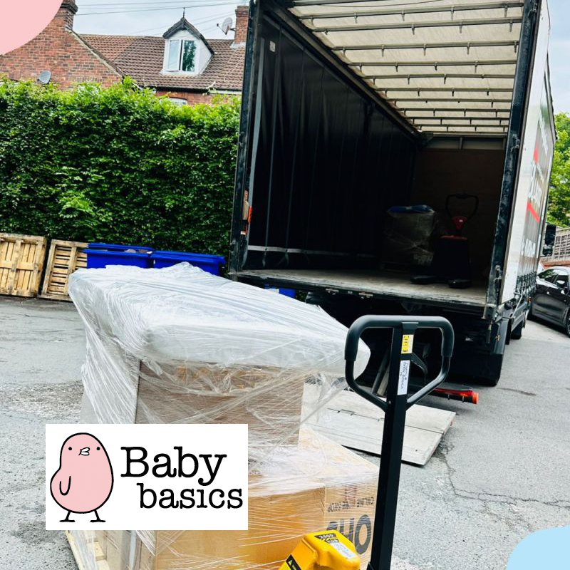 Pallet wrapped in plastic with cardboard boxes near an open delivery truck in a residential area.
