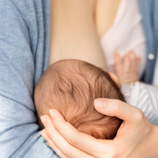 Close-up of a person gently cradling the head of a newborn baby with both hands.
