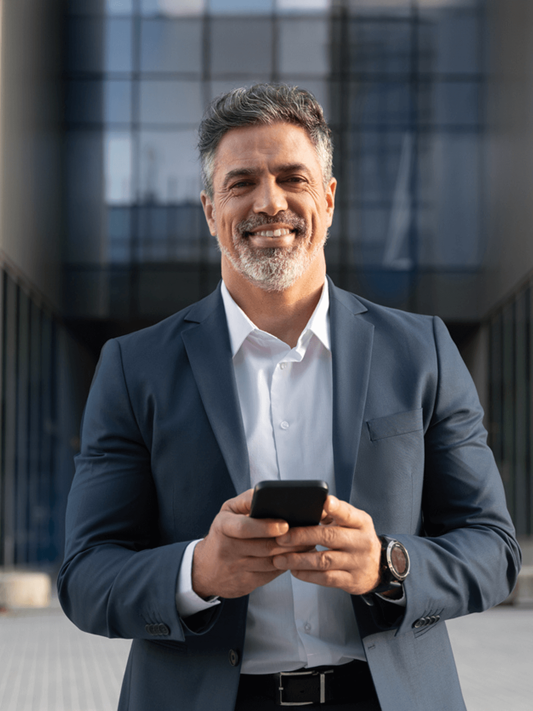 Mann im Anzug lächelnd, hält Smartphone, modernes Gebäude im Hintergrund.