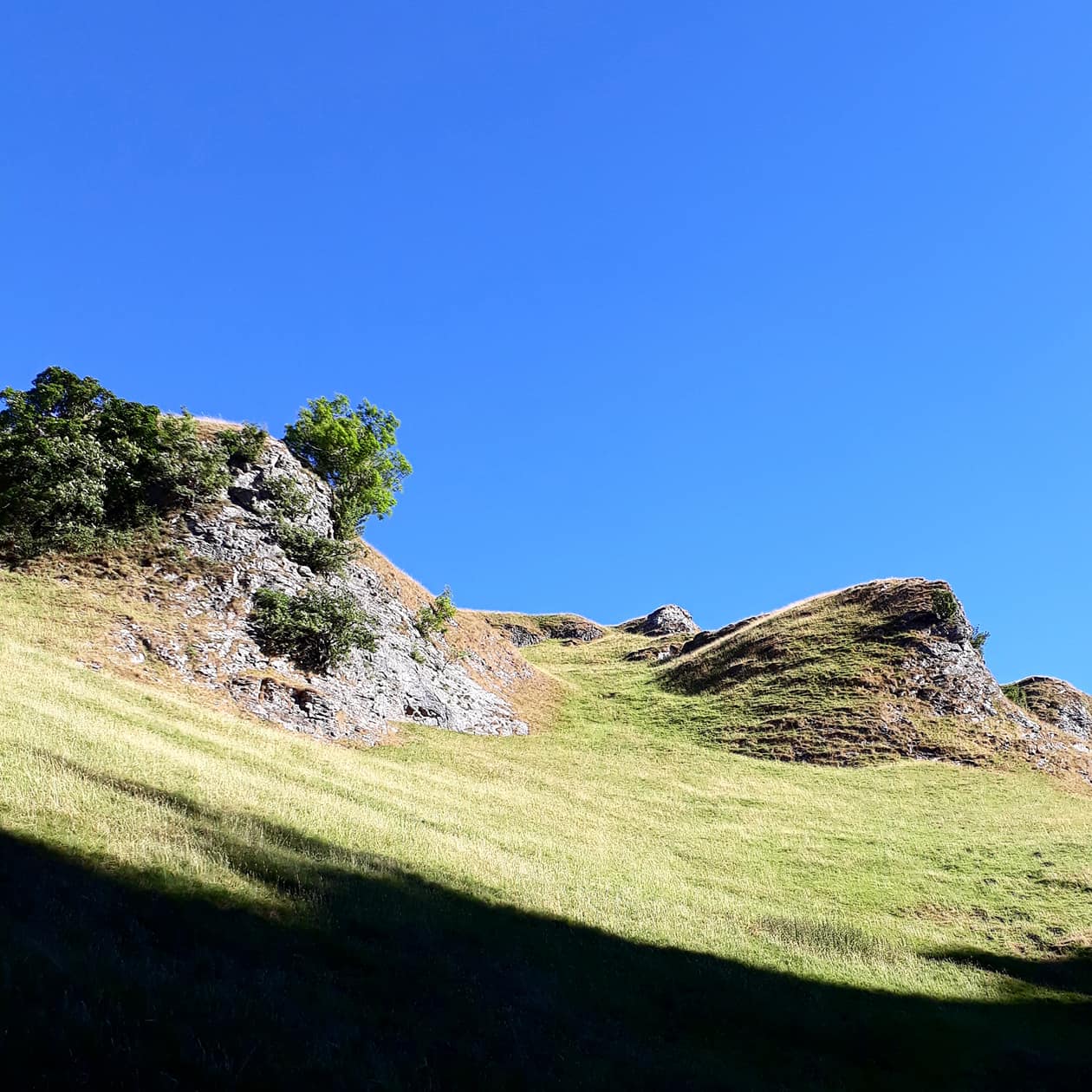 Landscape of the Peak District including clear blue sky, and rocks and bolders embedded into the grass.