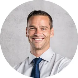 Smiling man with light skin and short hair wearing a black hoodie against a black background.