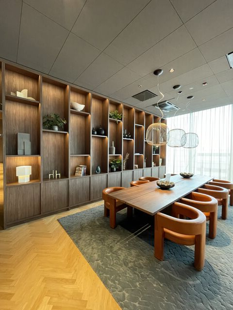 Modern dining room with long wooden table, six brown chairs, decorative shelves, and large windows with curtains.