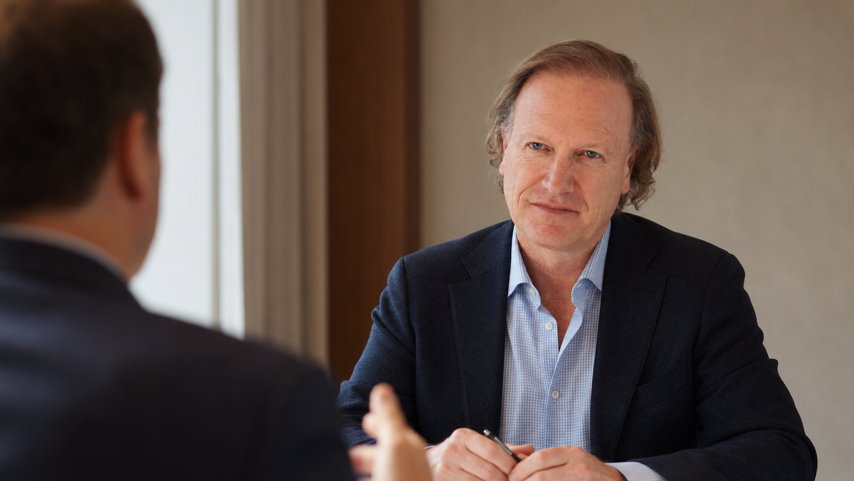 Man in a blue blazer listens attentively during a business interview.