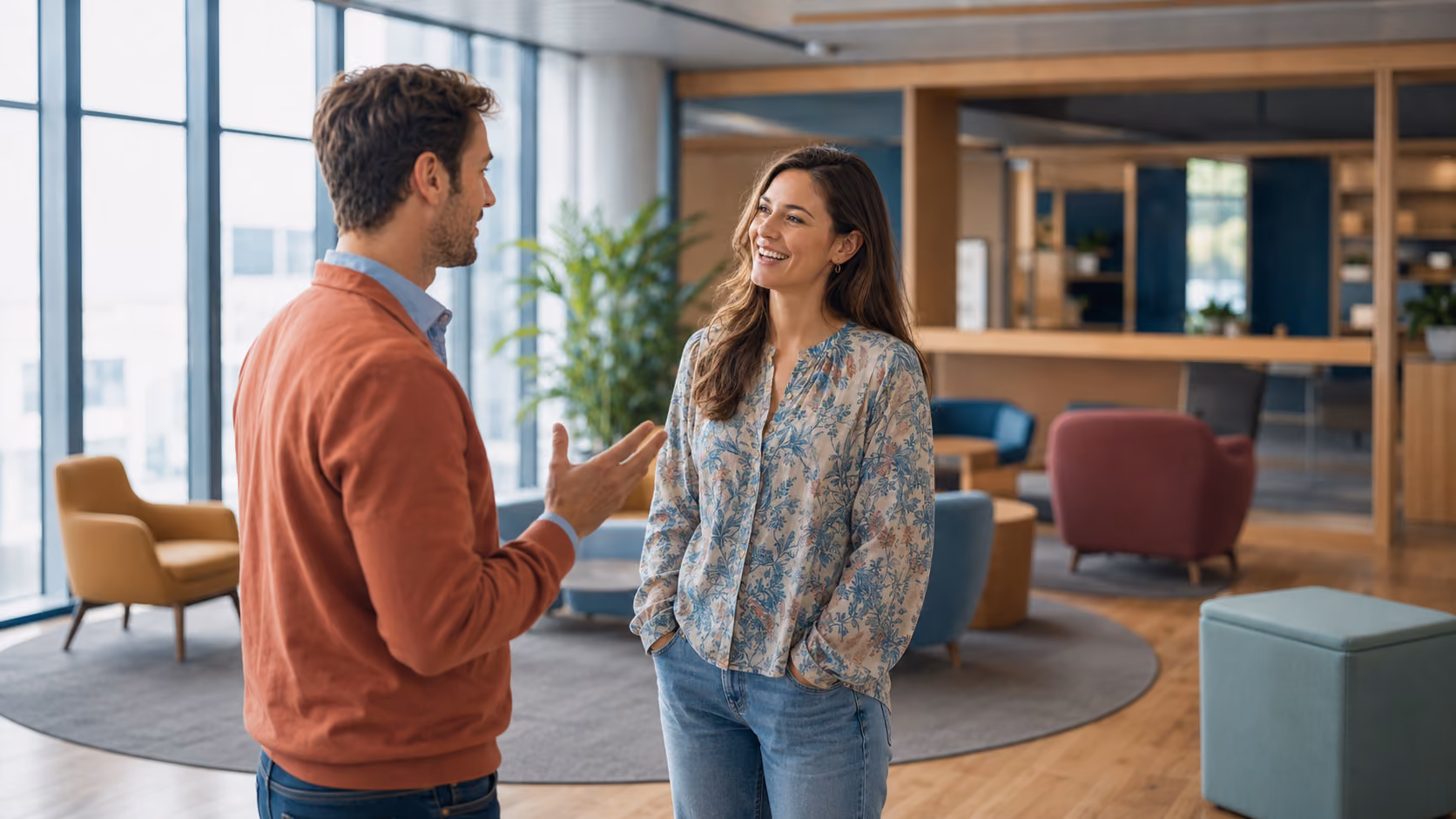 Smiling man and woman having a friendly conversation in a modern office lounge area.