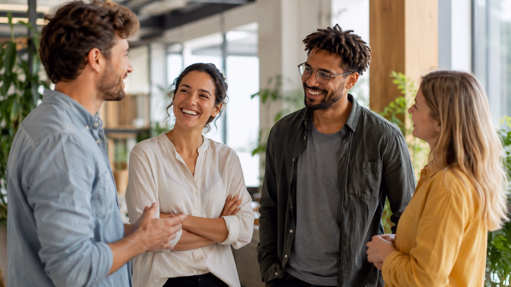 Four young adults standing indoors, engaged in a cheerful conversation with smiles and eye contact.