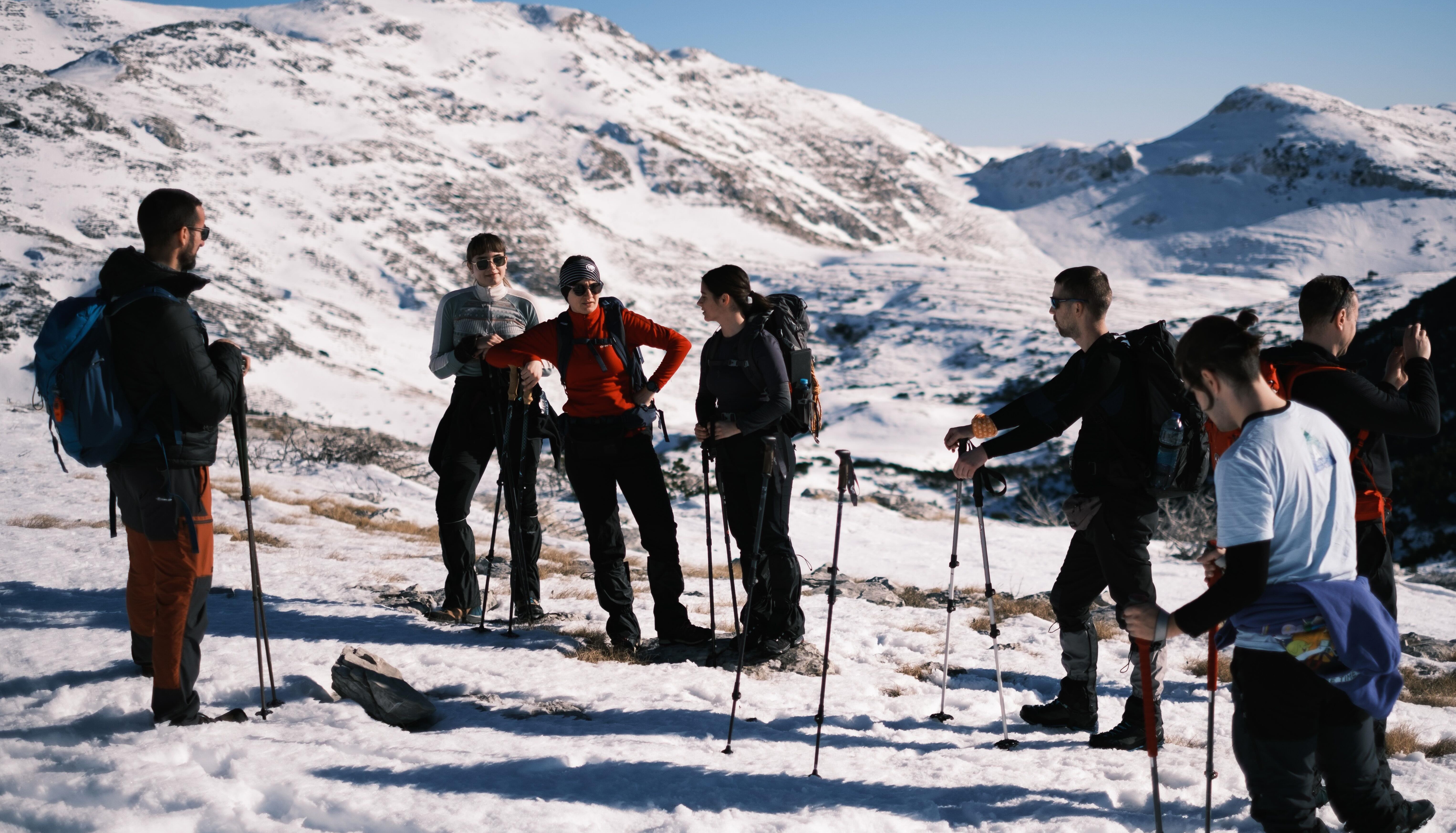 Group of hikers with poles resting on snowy mountain terrain under clear blue sky.