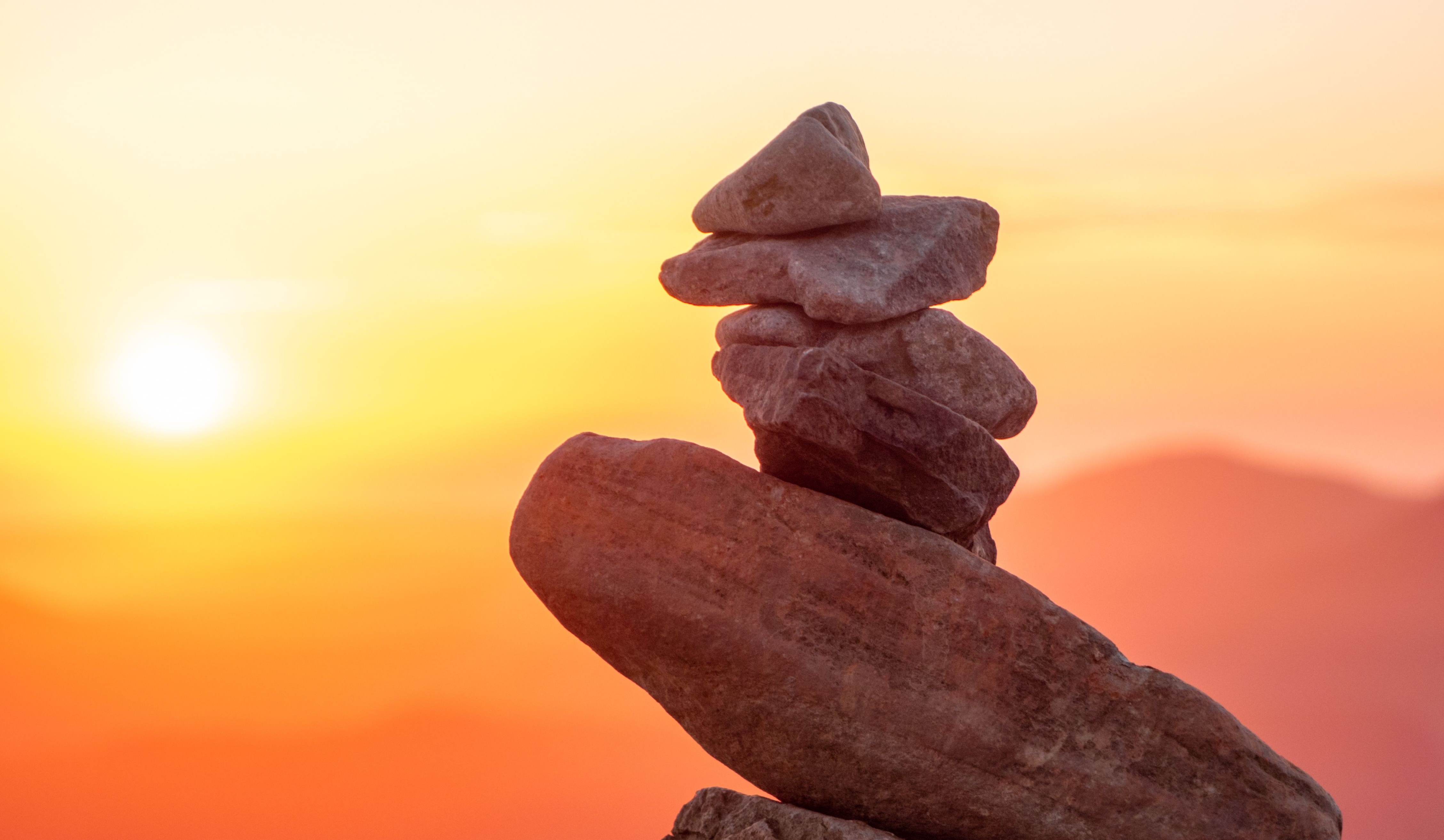 Stack of balanced rocks against a vibrant orange sunset with mountains in the background.