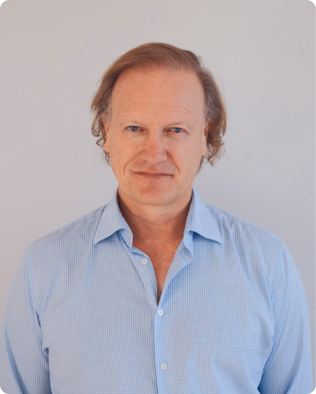 Middle-aged man with wavy light brown hair wearing a light blue checkered shirt against a plain background.