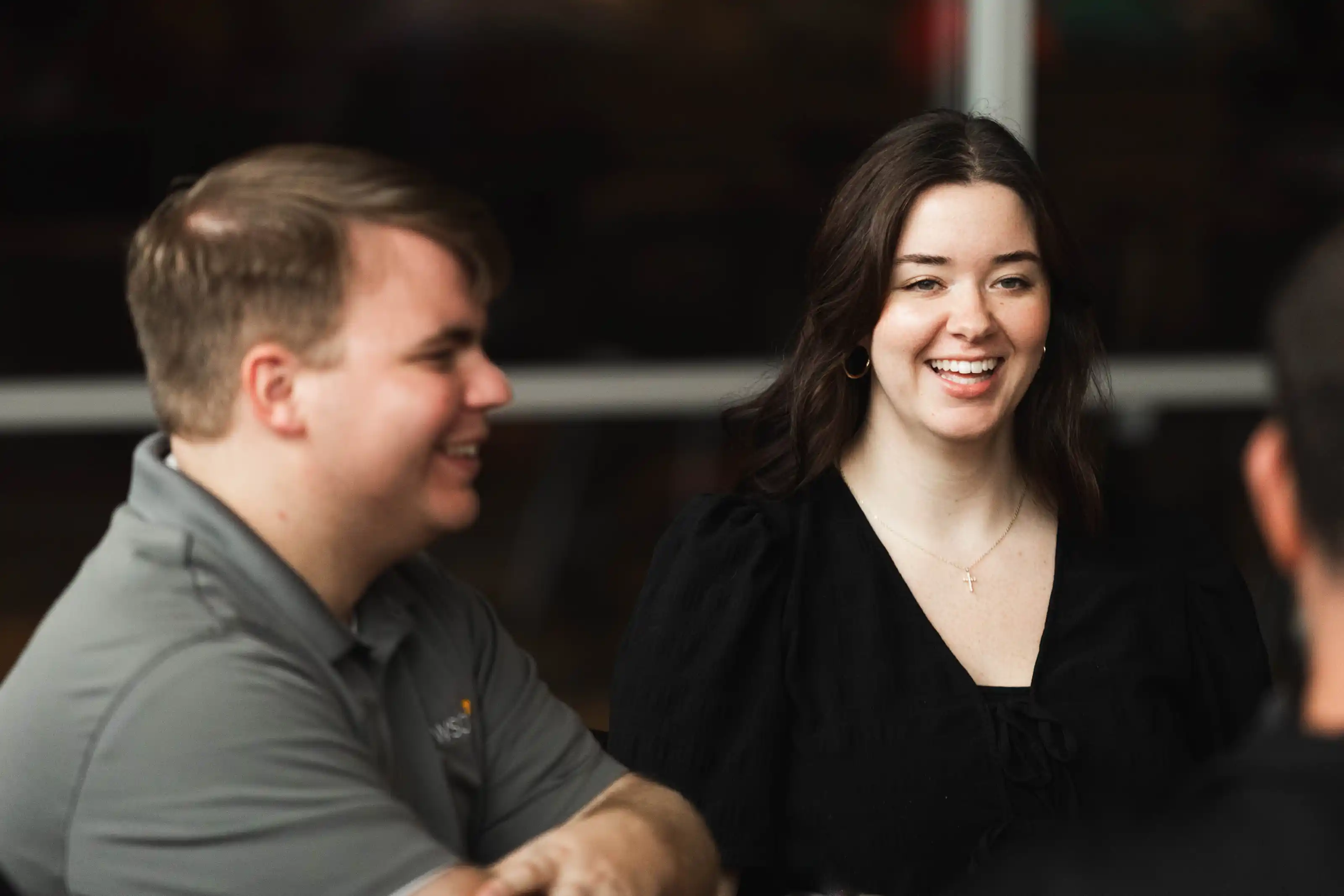 Two people sitting and smiling in a casual conversation, with a woman in a black top and a man in a gray shirt.