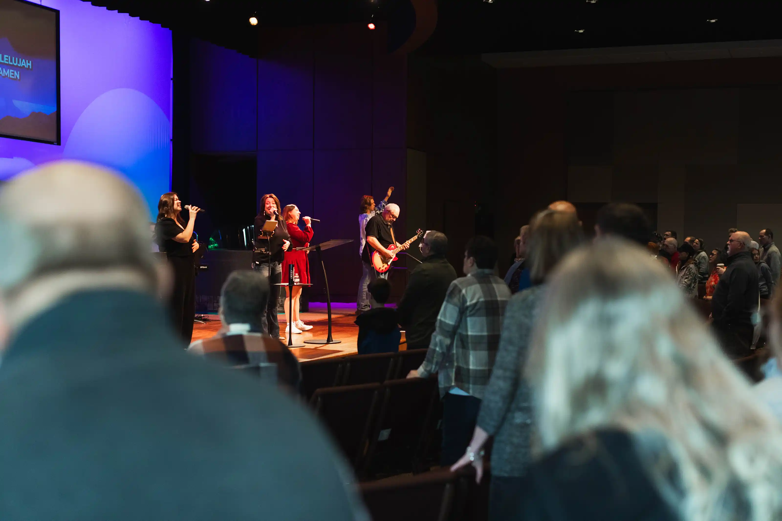 Congregation standing and singing during a church service with a worship band on stage.