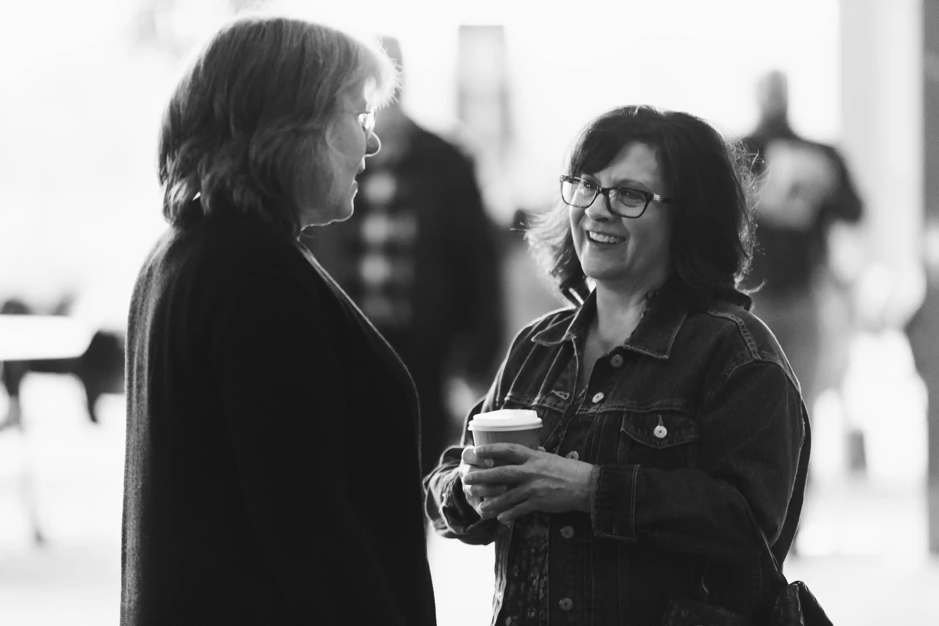 Two women engaged in a friendly conversation, one holding a coffee cup and smiling.