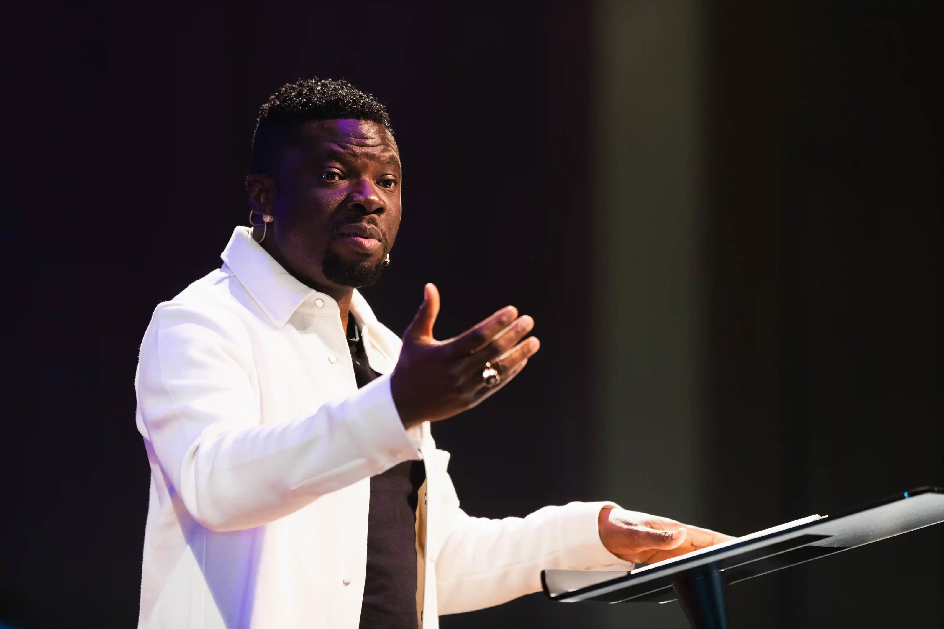Man speaking and gesturing with one hand while standing at a podium.