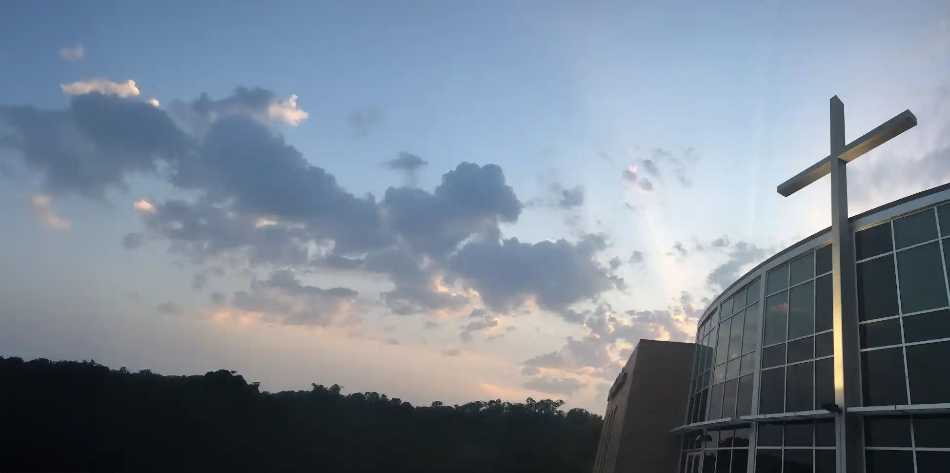 Modern church building with tall cross in front against a beautiful evening sky.