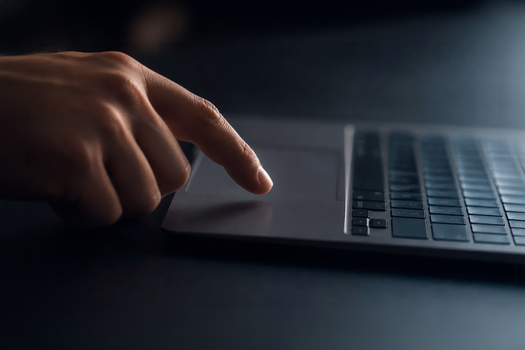 Hand hovering over a laptop trackpad in a moment of decision, illustrating the importance of low-friction CTAs on SaaS websites