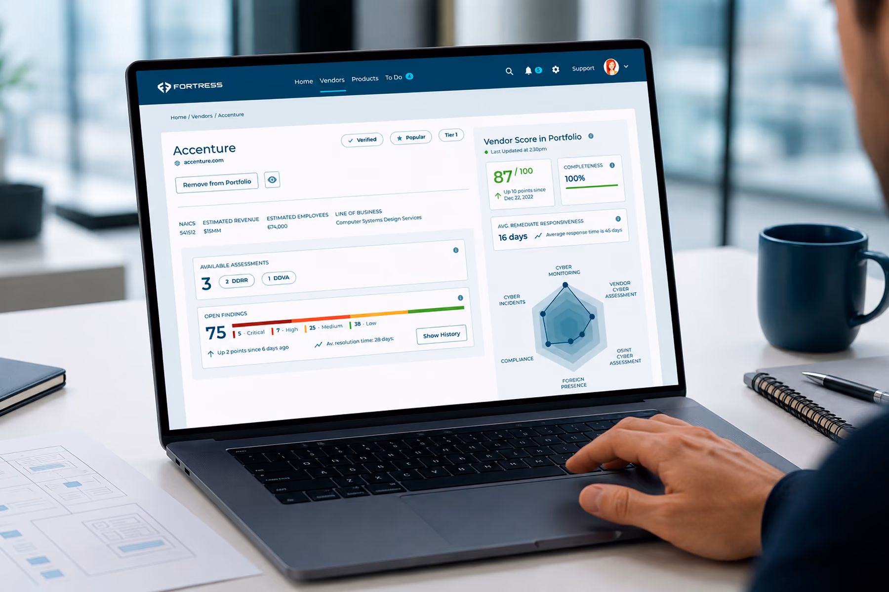 Laptop displaying a cybersecurity vendor dashboard in a modern office, with a professional’s hand near the trackpad and wireframe documents on the desk.