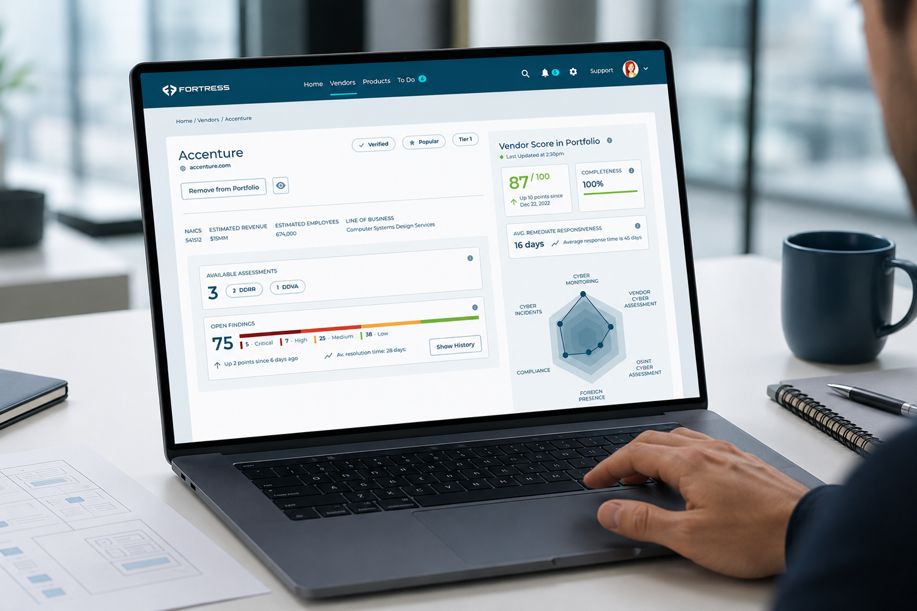 Laptop displaying a cybersecurity vendor dashboard in a modern office, with a professional’s hand near the trackpad and wireframe documents on the desk.