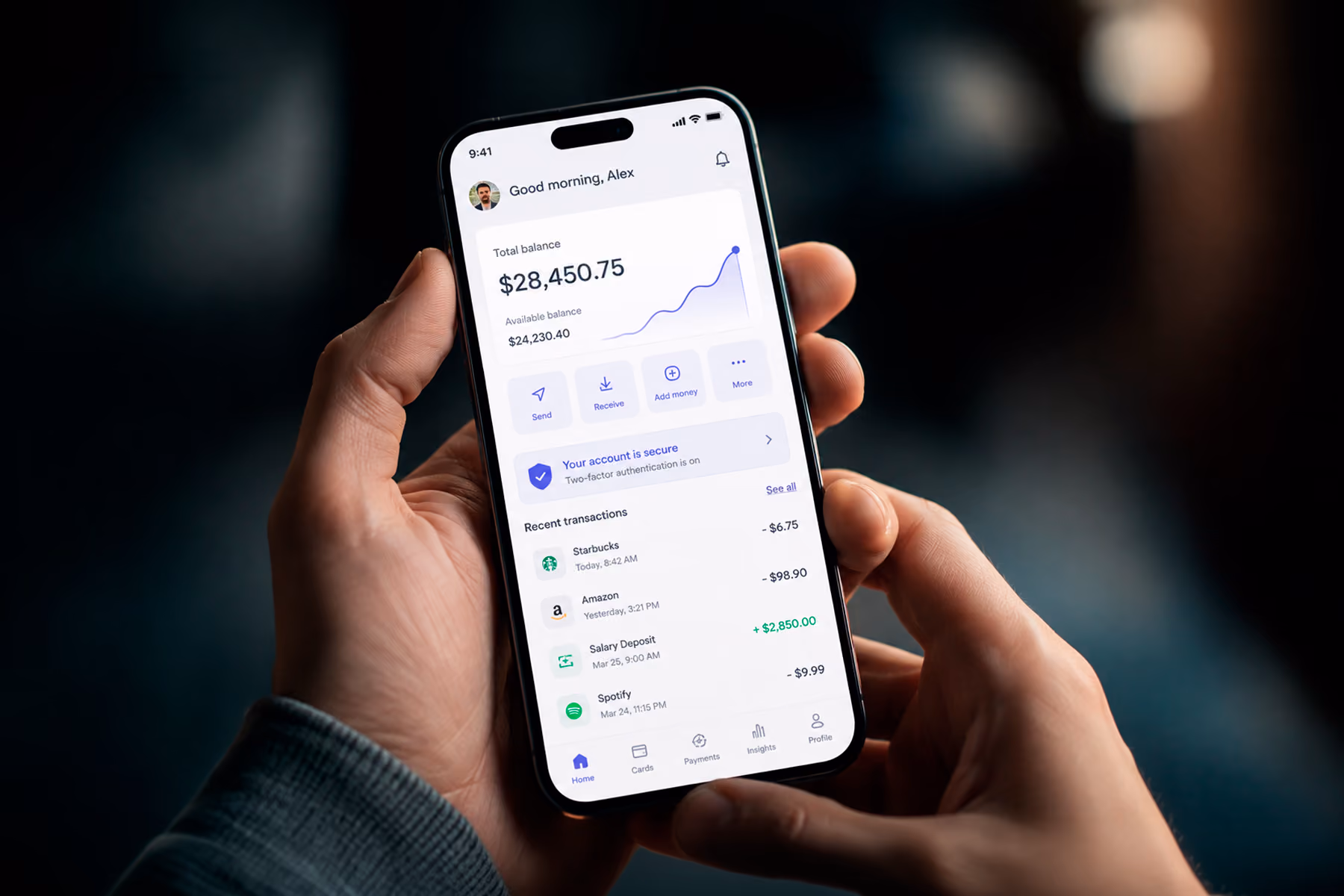 Hands holding smartphone displaying a modern fintech dashboard UI with account balance and transaction history