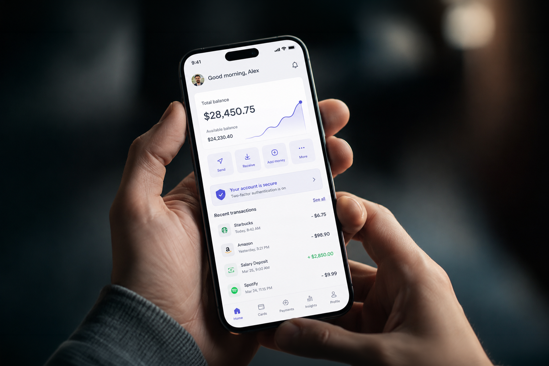 Hands holding smartphone displaying a modern fintech dashboard UI with account balance and transaction history