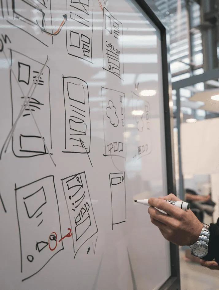 A UX architect sketching a website information architecture wireframe on a whiteboard in a modern design studio.