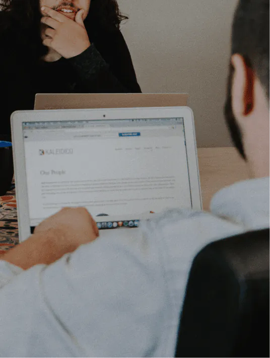 Startup team reviewing a mobile app interface and discussing UX design improvements on a laptop and smartphone screens