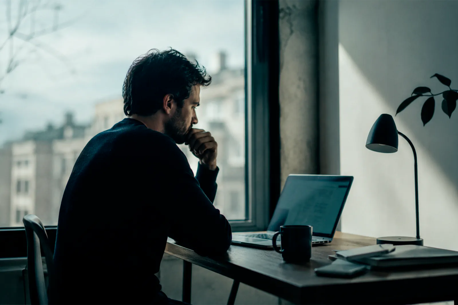 Startup founder sitting alone at a desk deep in thought, looking at a laptop screen