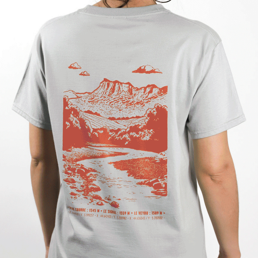 Personne portant un t-shirt gris avec une illustration orange d’un paysage montagneux et une rivière au dos, avec des noms et altitudes de sommets en bas.