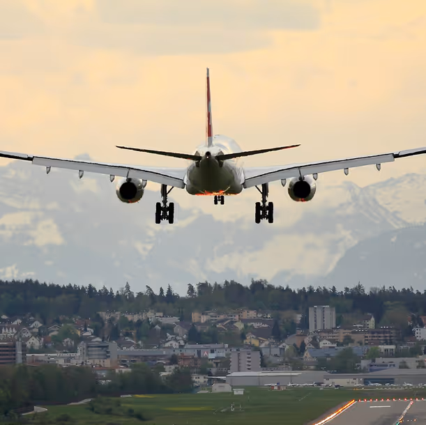 Avion en approche d'atterrissage au-dessus d'une piste avec une ville et des montagnes en arrière-plan.