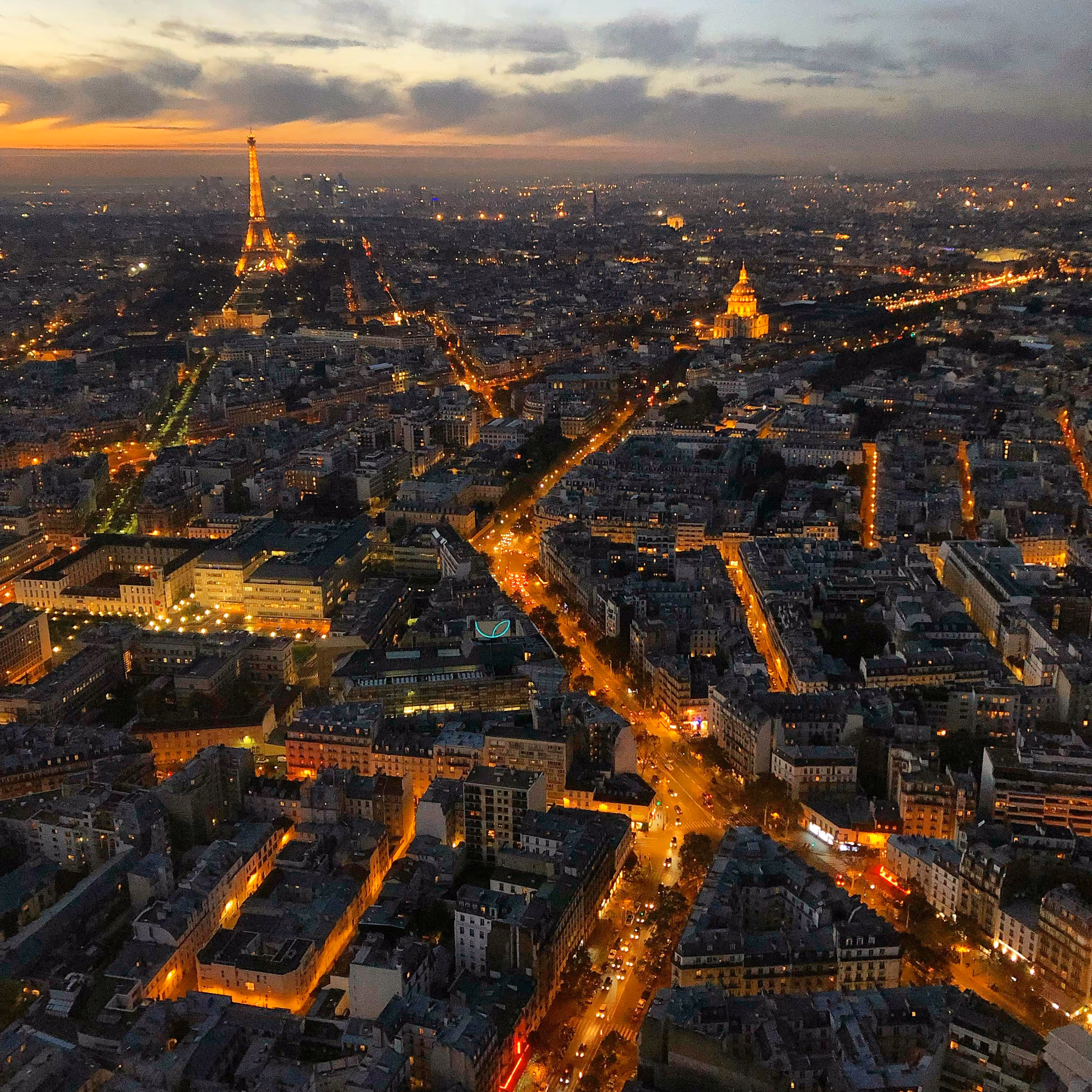 Vue aérienne de nuit de Paris avec la tour Eiffel illuminée à gauche et les rues éclairées s'étendant dans la ville.