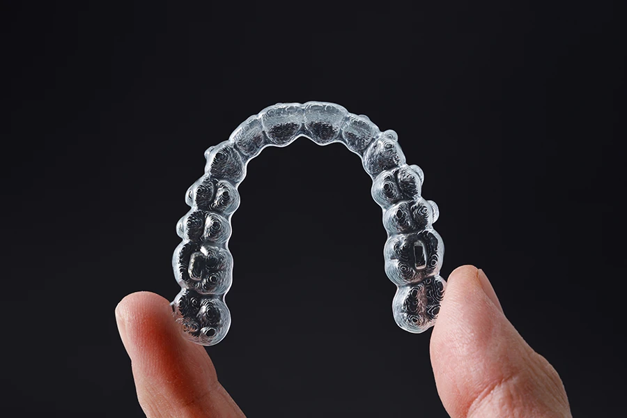 Close-up of a hand holding a clear dental aligner against a dark background.