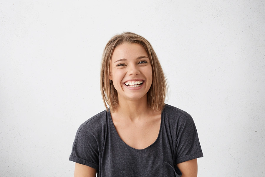 Smiling young woman with shoulder-length light brown hair wearing a dark gray t-shirt against a plain white background.