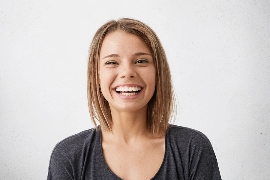 Smiling young woman with straight short brown hair wearing a dark gray shirt against a light background.