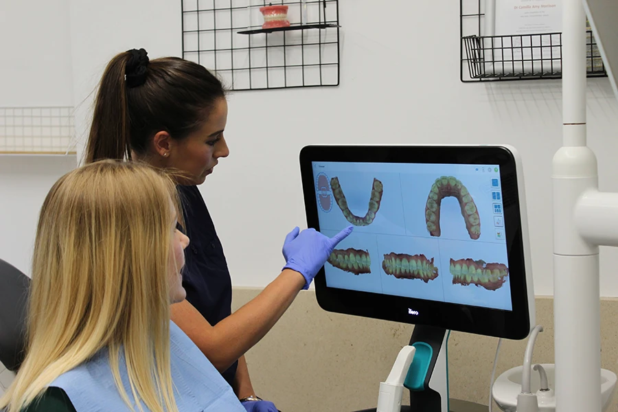 Dental professional explaining 3D digital images of teeth to a patient on a monitor.