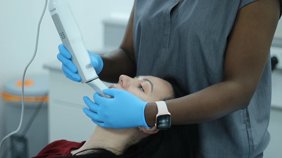 Dental professional wearing blue gloves performing a mouth scan on a patient using an intraoral scanner.