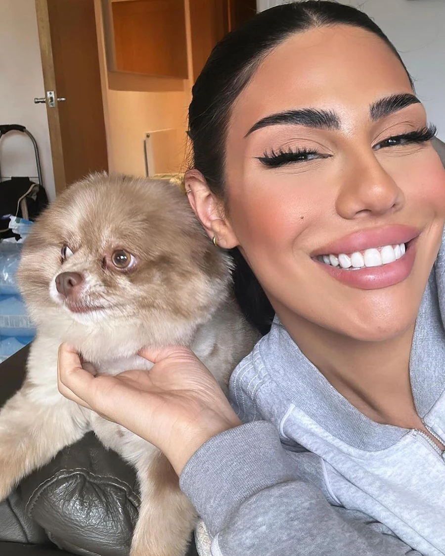 Smiling woman holding a fluffy light brown dog while sitting on a couch.