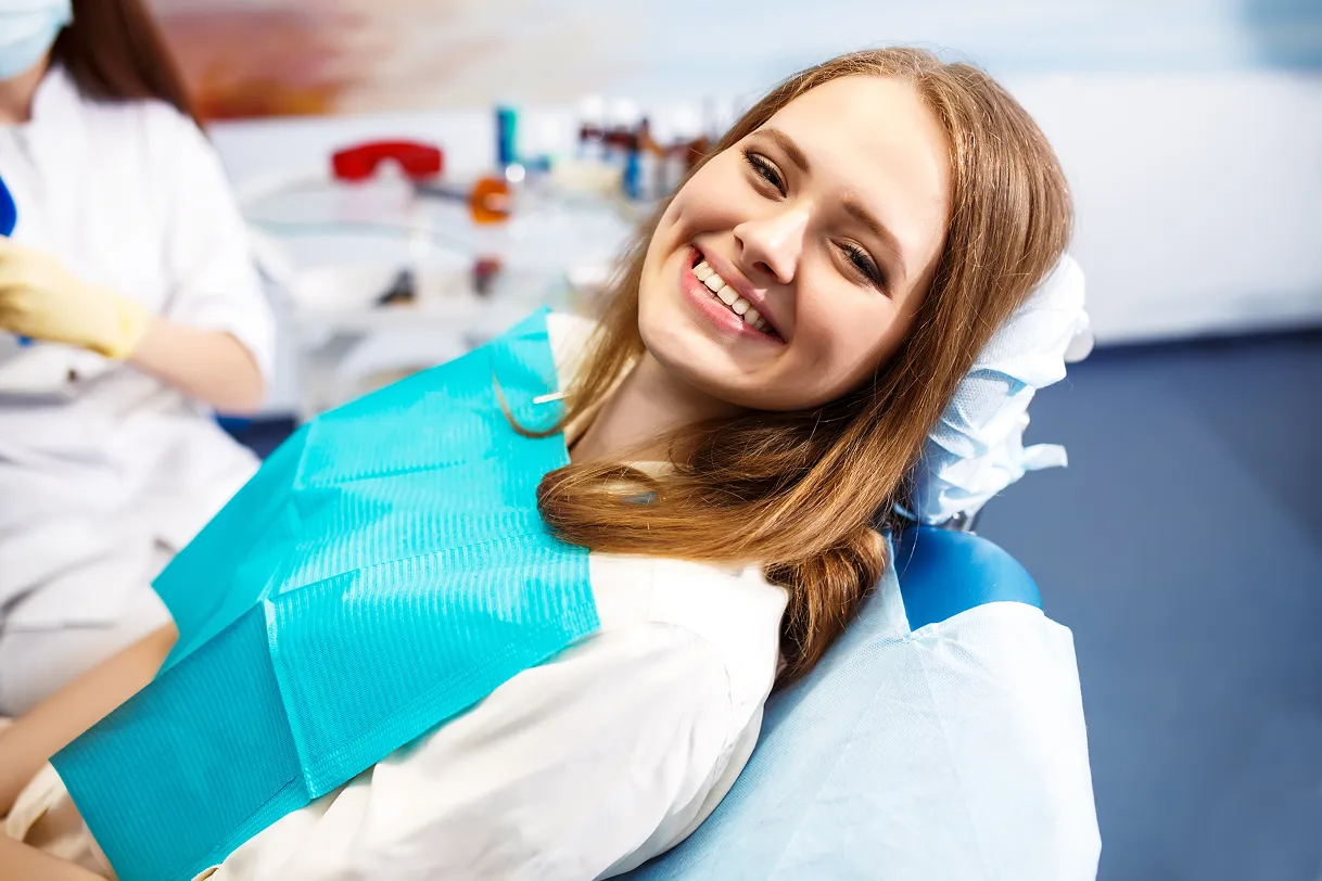 Smiling young woman sitting in a dental chair wearing a blue dental bib.