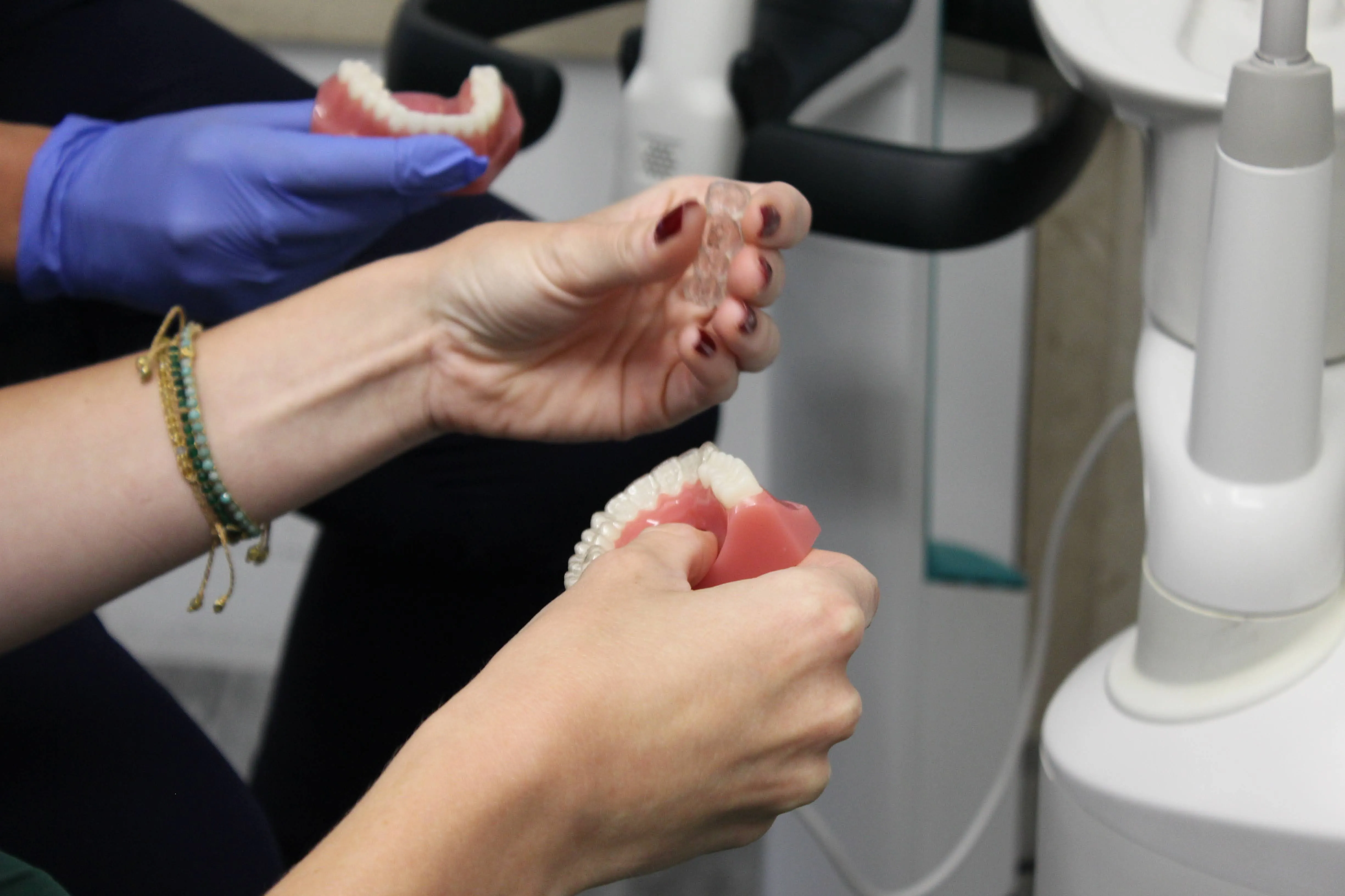 Two people holding dental models and a clear aligner inside a dental clinic.