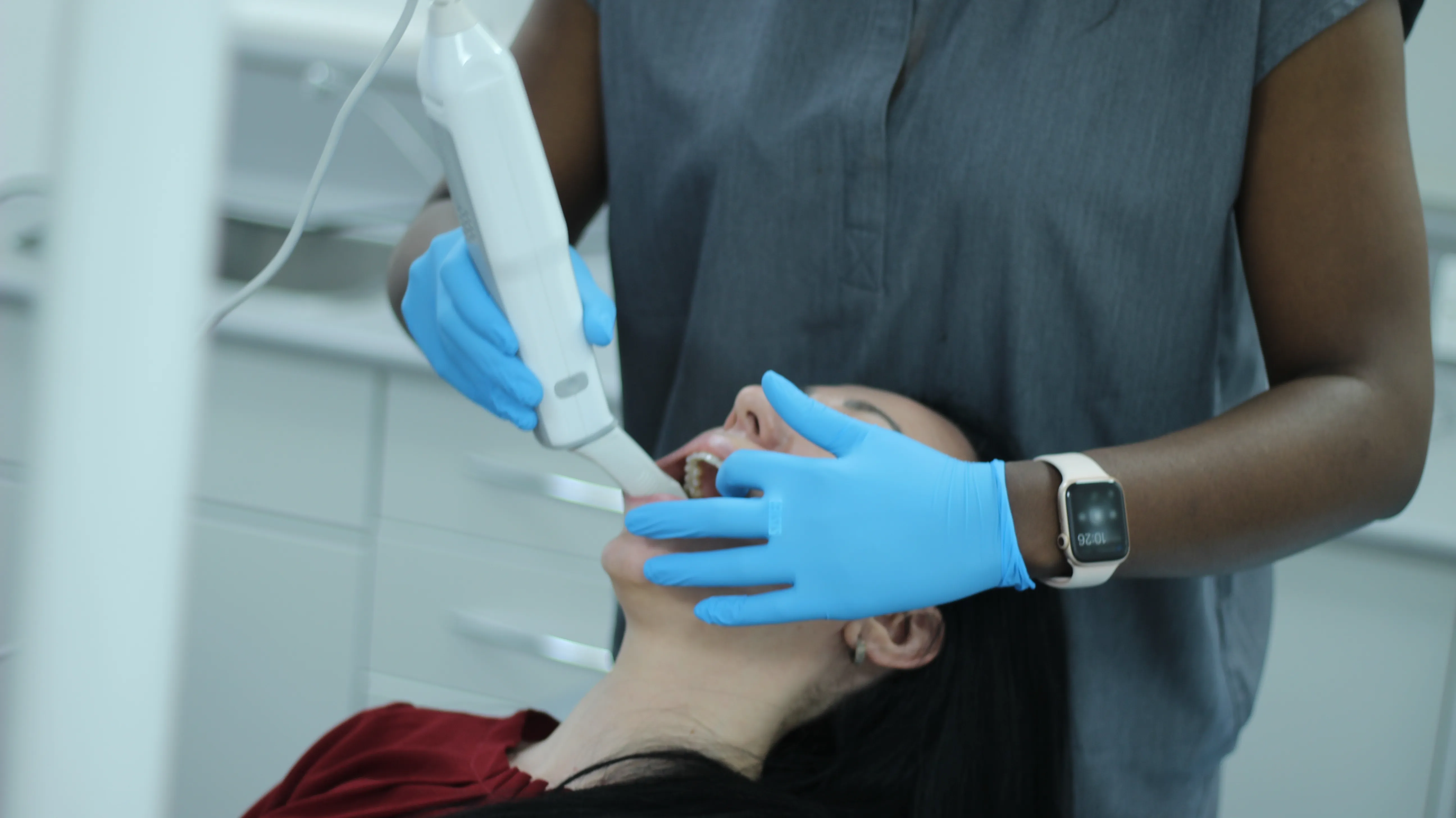Dentist wearing blue gloves scanning a patient's teeth with an intraoral scanner in a dental clinic.