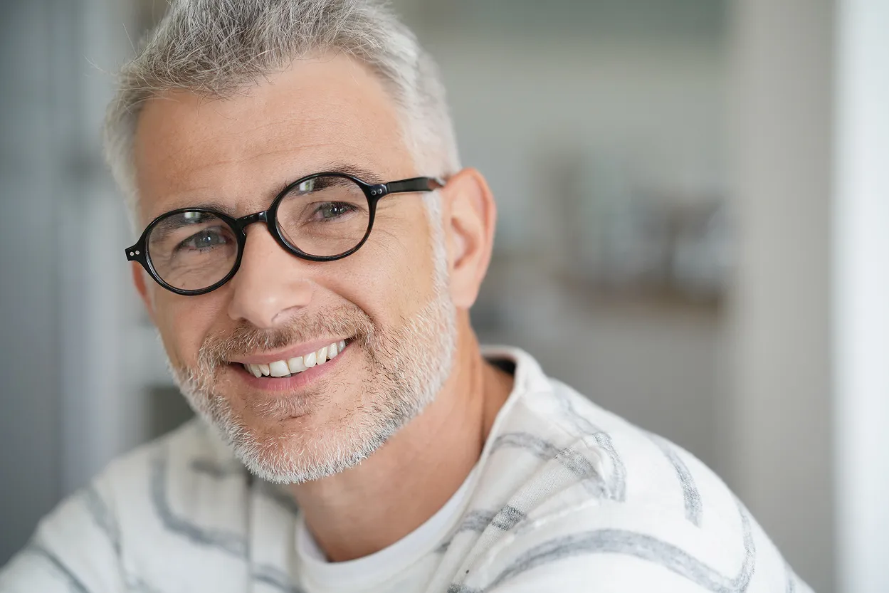 Smiling middle-aged man with gray hair and beard wearing round black glasses and a white striped shirt.