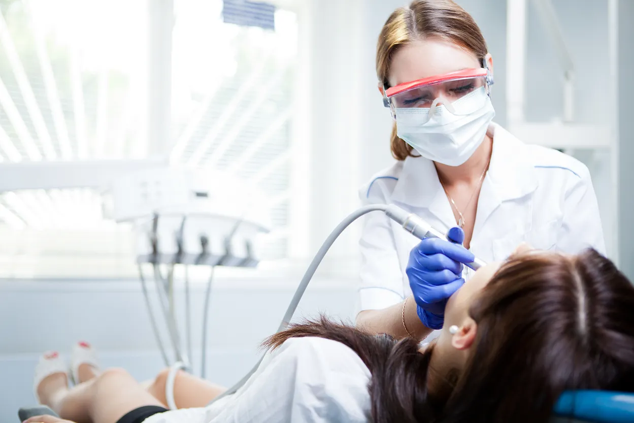 Dentist wearing protective mask and goggles treating a patient reclining in a dental chair.