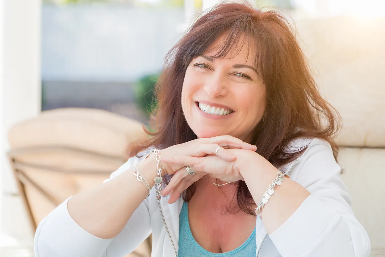 Smiling middle-aged woman with brown hair resting her chin on her hands outdoors.