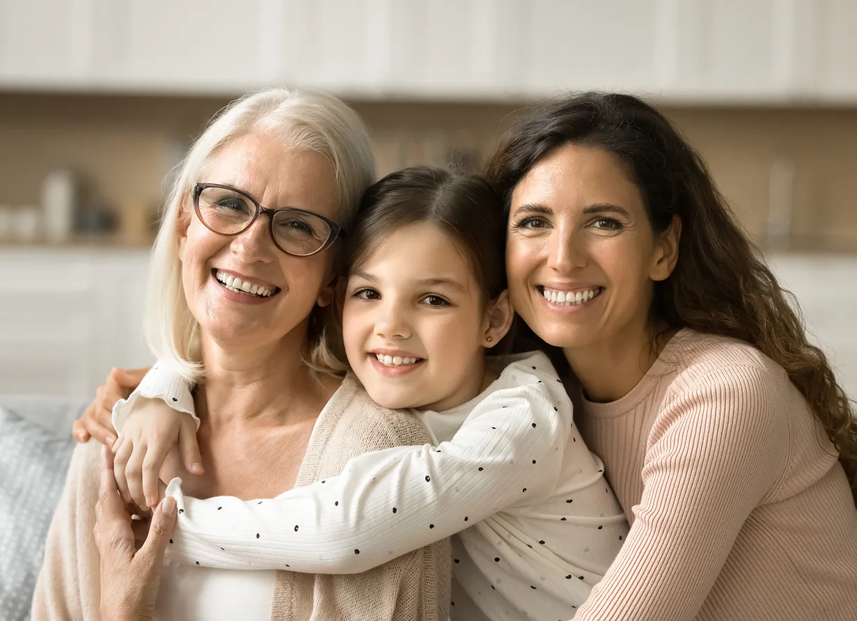 Three generations of women smiling and hugging each other in a cozy home setting.