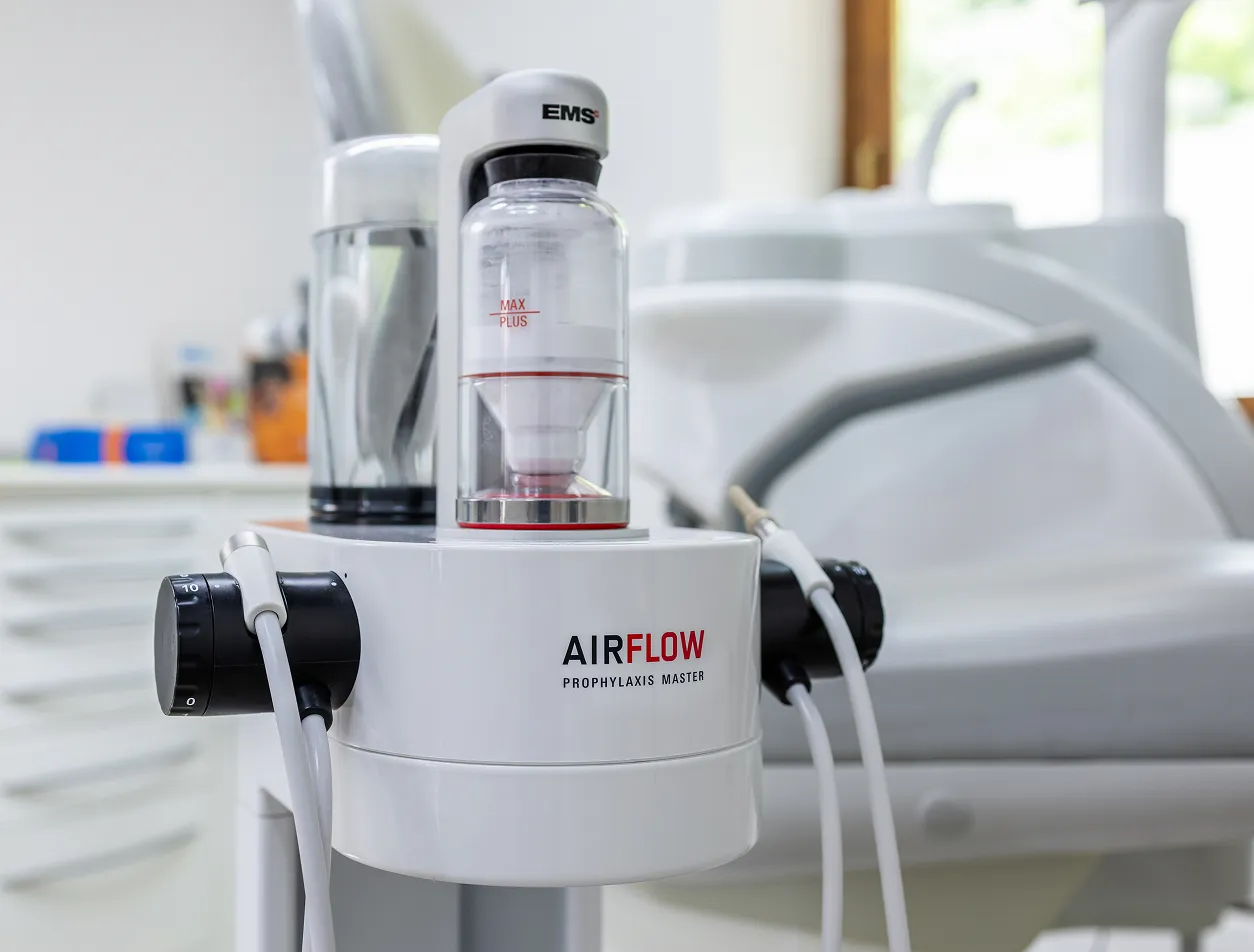 Close-up of an AIRFLOW Prophylaxis Master dental cleaning device with connected hoses in a dental clinic.