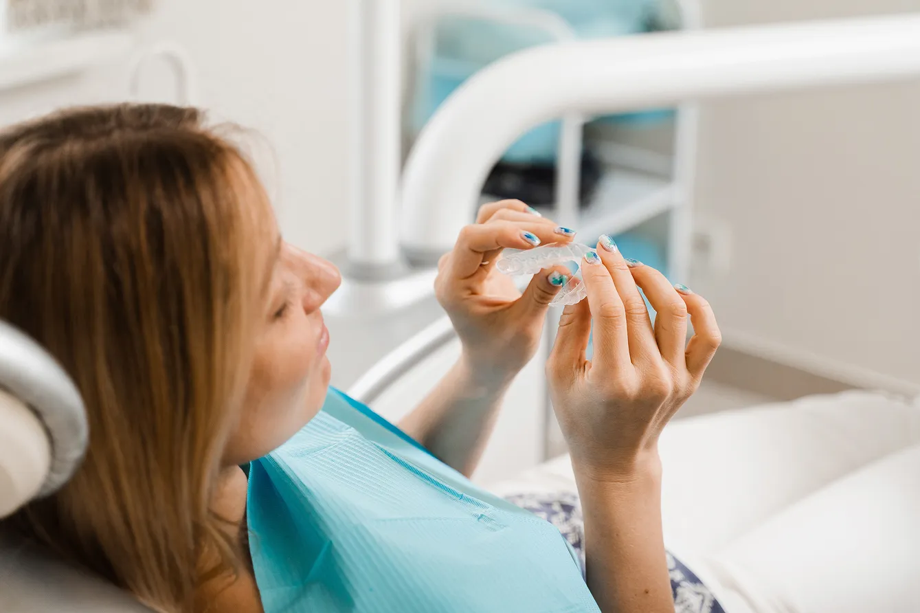 Woman in dental chair holding and inspecting a clear dental aligner.